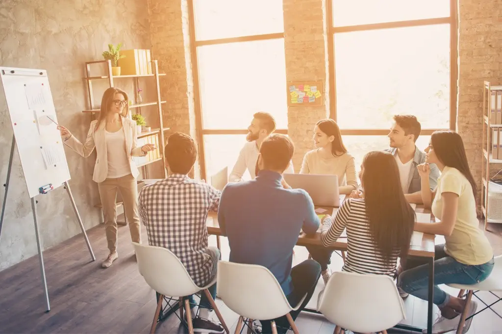 Corsi professionali Areajob - donna che sta spiegando una sua strategia ai colleghi durante una riunione e sono tutti seduti al tavolo ad ascoltarla